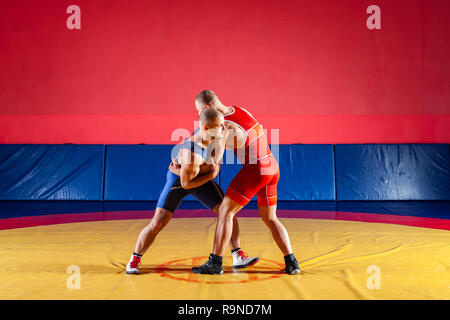 Le concept de la juste lutte. Deux lutteurs gréco-romain en rouge et bleu sur un uniforme jaune wrestling lutte tapis dans la salle de sport Banque D'Images