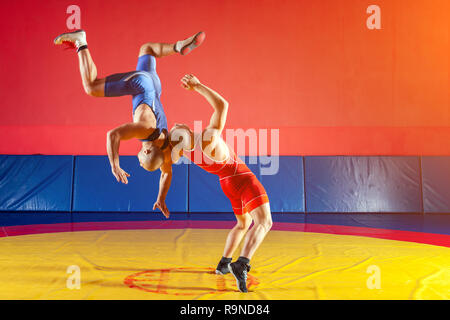 Deux lutteurs forte en bleu et rouge wrestling collants sont wrestlng et faire une suplex wrestling wrestling jaune sur un tapis dans la salle de sport. Jeune homme ne Banque D'Images