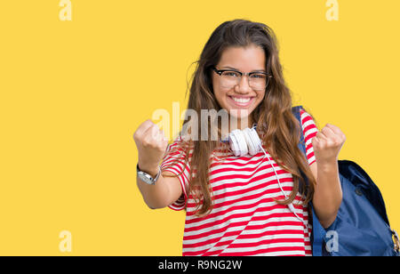 Jeune étudiante belle brunette woman wearing headphones et son sac à dos sur fond isolé très heureux et excité de faire geste gagnant avec armoiries Banque D'Images