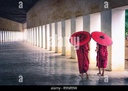 Deux moine novice tenant un parapluie rouge et de la marche dans la pagode, le Myanmar. Banque D'Images