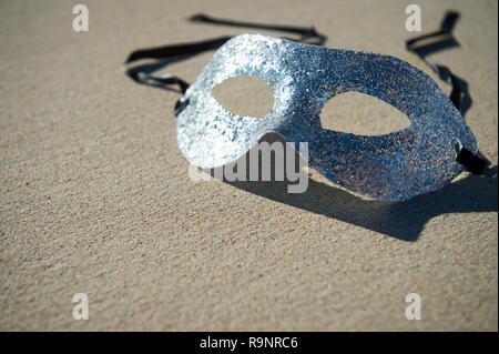 Masque de carnaval argent étincelant en attente dans le soleil tropical sur sable texturé à Rio de Janeiro, Brésil Banque D'Images