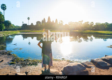 Un touriste en visite des ruines d'Angkor Vat au lever du soleil, voyage destination Cambodge. Réflexion sur l'eau étang et sunburst, Femme au chapeau traditionnel et r Banque D'Images