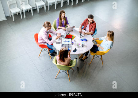 Une équipe de jeunes collègues habillés de désinvolture qui travaillent ensemble avec des ordinateurs portables assis à la table ronde dans le bureau, vue de dessus Banque D'Images