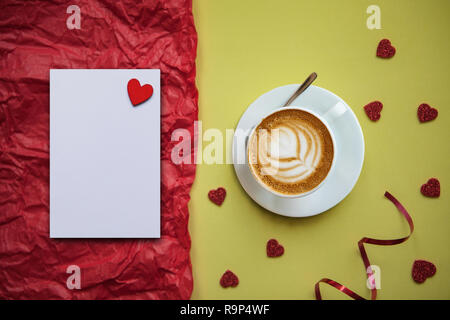 Une tasse de cappuccino aromatisé café sur un fond de fête avec beaucoup de cœurs. À côté d'une feuille blanche avec un coeur pour des textes ou des félicitations. Célébration de la Saint Valentin ou la Journée de la femme ou autre événement d'amour. Banque D'Images