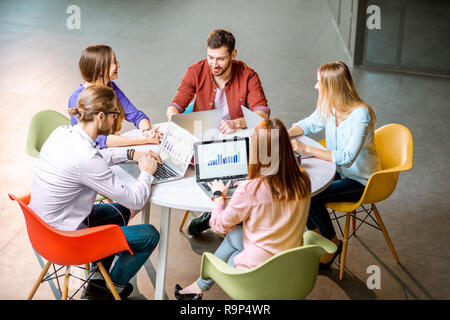Une équipe de jeunes collègues habillés de désinvolture qui travaillent ensemble avec des ordinateurs portables assis à la table ronde de l'office Banque D'Images