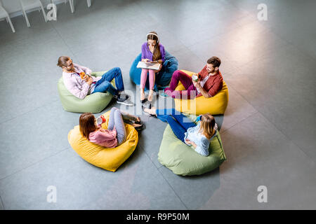 Un groupe de jeunes collègues assis ensemble sur les poufs colorés se reposer pendant la pause café au bureau, vue d'en haut Banque D'Images
