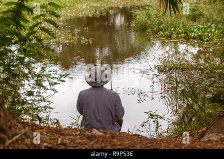 Un homme dans un chapeau jette une canne à pêche sur un petit étang, pêche dans l'étang Banque D'Images