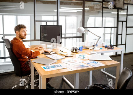 L'homme comme un programmeur travaillant avec un code informatique assis à la belle place de travail dans l'intérieur de bureau moderne Banque D'Images