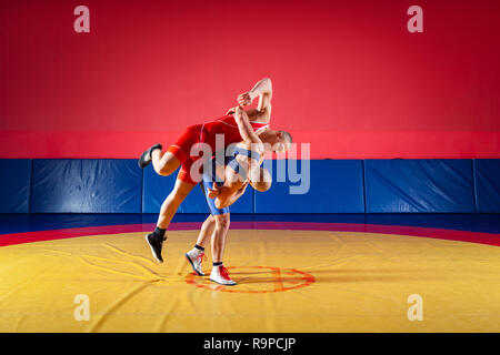 Deux jeunes hommes en bleu et rouge wrestling collants sont wrestlng et faire un jet de hanche sur un tapis de lutte jaune dans la salle de sport. La notion de juste wrestl Banque D'Images