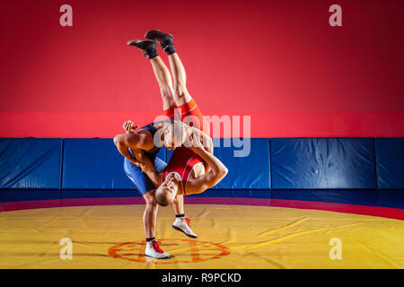 Le concept de la juste lutte. Deux jeunes hommes en bleu et rouge wrestling collants sont wrestlng et faire une suplex wrestling sur un tapis de lutte jaune Banque D'Images