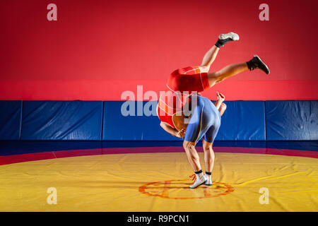 Le concept de la juste lutte. Deux jeunes hommes en bleu et rouge wrestling collants sont wrestlng et faire une suplex wrestling sur un tapis de lutte jaune Banque D'Images