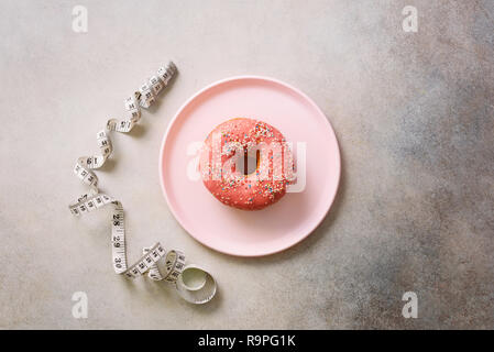 Donut rose sur la plaque, ruban à mesurer sur fond de béton gris. Concept de régime. Le poids perdu après les vacances. Banque D'Images