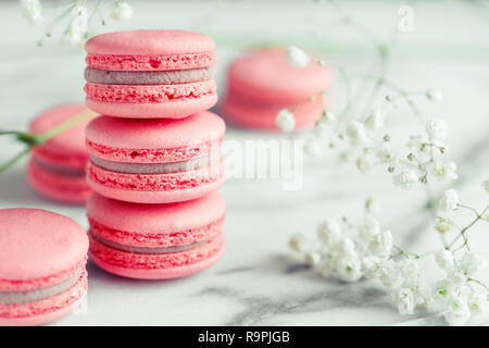 Pile de gâteaux macarons macarons de corail ou sur du marbre blanc avec des fleurs en plus. Banque D'Images