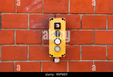 L'interrupteur jaune industriel fort avec l'appareil sous et hors tension de blocage des boutons et des interrupteurs installés à l'extérieur sur un mur de brique rouge de l'entrepôt. Banque D'Images