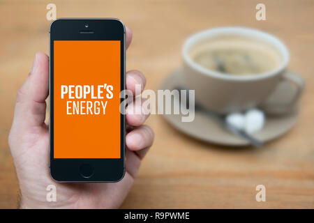 Un homme se penche sur son iPhone qui affiche le logo de l'énergie du peuple (usage éditorial uniquement). Banque D'Images