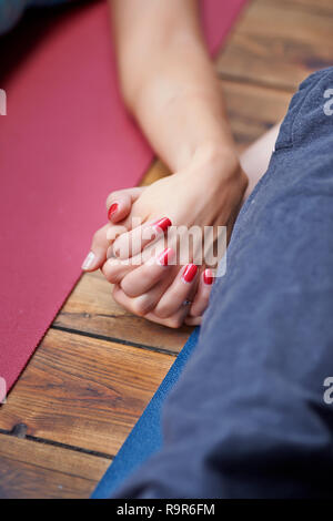 Jeune femme de détente sur le plancher en bois en shavasana et tenir la main. Banque D'Images