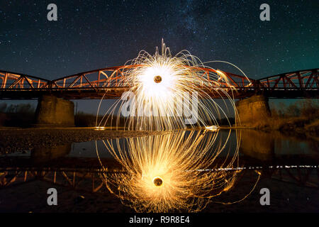 La lumière peinture art concept. La filature de la laine d'acier en résumé, cercle de douches d'artifice lumineux jaune vif brille sur long pont reflète dans riv Banque D'Images