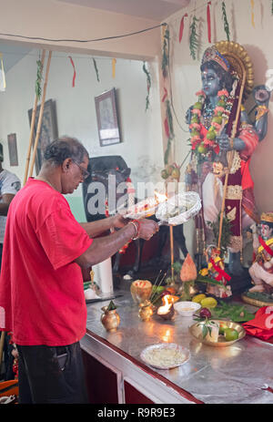 L'ARTI rituel. Un hindou pieux avec l'homme est la tête inclinée prie et vague feu devant une statue d'une divinité dans un temple dans le Queens, New York. Banque D'Images