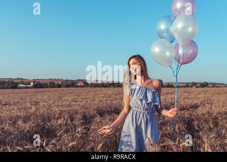 La jeune fille dans le champ journée ensoleillée. Dans les mains de holding balloons. Sourit joyeusement et se penche sur la distance. Espace libre pour le texte. Le concept de don et de vacances. Plaisir d'émotions le plaisir et la joie. Banque D'Images