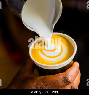 Café Barista pouring africains une forme des feuilles avec de la mousse de lait dans une tasse à emporter Banque D'Images