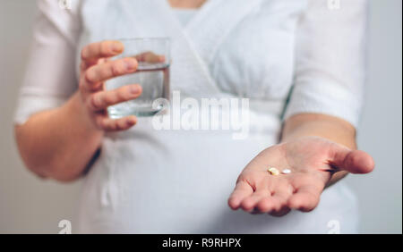 Méconnaissable pregnant woman showing pills et tenant un verre d'eau Banque D'Images