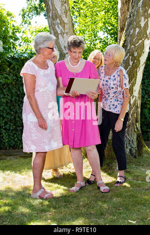 Groupe de professionnels seniors femmes à la recherche de photo d'une femme tient dans ses mains, debout à l'extérieur dans le parc en été. Banque D'Images