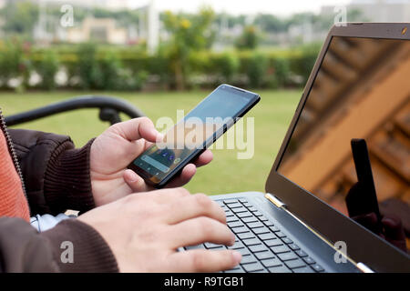 Boy est holding smartphone dans la main avec l'ordinateur portable. Banque D'Images