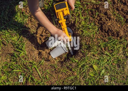 Le garçon joue le recyclage. Il enterre des plats jetables en plastique et biodégradable vaisselle Banque D'Images