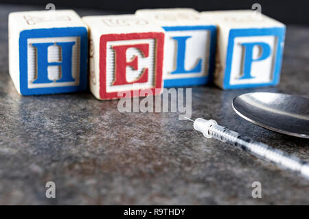 Cuillère et seringue en premier plan avec 'Aide' énoncés dans des blocs à l'arrière-plan flou. Conceptual de suggérer l'usage de drogues illicites et demander de l'hôtel Banque D'Images