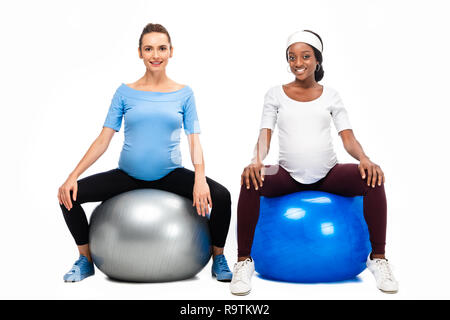 Deux femmes enceintes multiculturelle assis sur des boules de forme physique isolated on white Banque D'Images