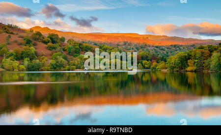 Coucher du soleil d'automne à la recherche à travers le miroir reflet dans l'eau à Rydal Boat House & the golden fells dans la distance. Banque D'Images