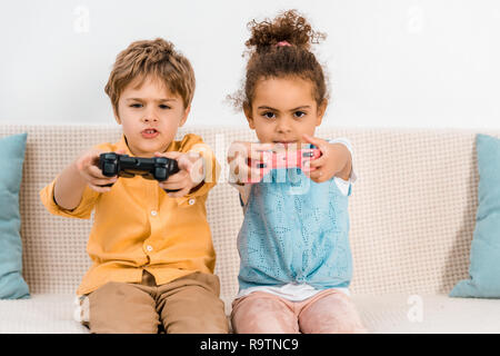 Adorable Kids playing video game multiethnique avec joysticks et looking at camera Banque D'Images
