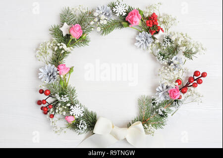 Maquette de couronne de Noël faites de branches de Pins à la recherche naturaliste décoré de fruits rouges. Mise à plat sur un fond de bois blanc, avec place pour votre texte. Vue d'en haut Banque D'Images