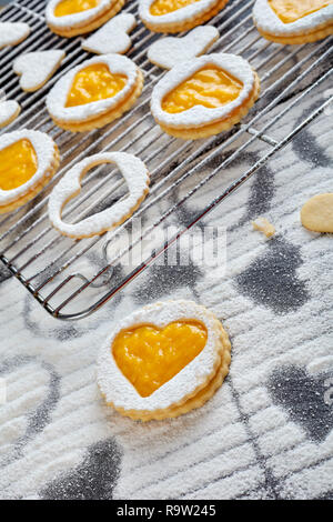 Linzer cookies en forme de coeur avec mangue bio saupoudrée de sucre en poudre sur une grille sur une table en bois noir, vertical Vue de dessus Banque D'Images