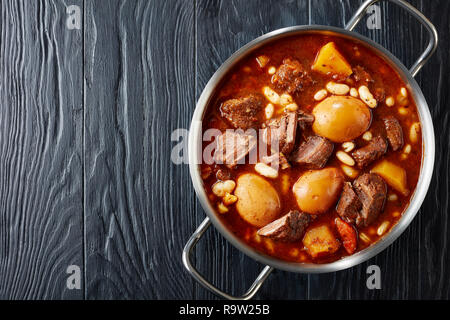 Juif traditionnel Tcholent (Hamin) - plat principal pour le repas de Chabbat lent boeuf cuit avec des pommes de terre, haricots et brun oeufs dans une casserole de métal sur un fond noir Banque D'Images