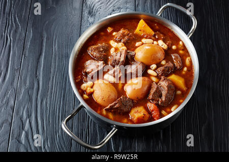 Juif traditionnel Tcholent (Hamin) - plat principal pour le Shabbat lunc, lent boeuf cuit avec des pommes de terre, haricots et brun oeufs dans une casserole de métal sur un blac Banque D'Images