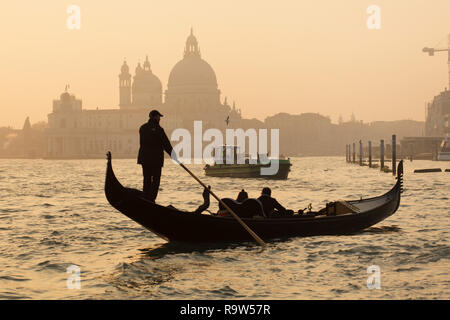 En gondole à coucher de soleil dans la lagune de Venise (Laguna di Venezia) en face de la Basilique de Santa Maria della Salute (Basilica di Santa Maria della Salute) à Venise, Italie. La collecte des ordures le bateau est vu dans l'arrière-plan. Banque D'Images