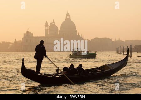 En gondole à coucher de soleil dans la lagune de Venise (Laguna di Venezia) en face de la Basilique de Santa Maria della Salute (Basilica di Santa Maria della Salute) à Venise, Italie. La collecte des ordures le bateau est vu dans l'arrière-plan. Banque D'Images