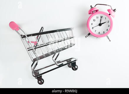 Shopping femmes temps. Panier et réveil couleur rose sur un fond blanc. Banque D'Images