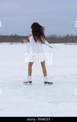 Belle jeune femme sur patins en robe blanche à l'extérieur à l'hiver neige Banque D'Images