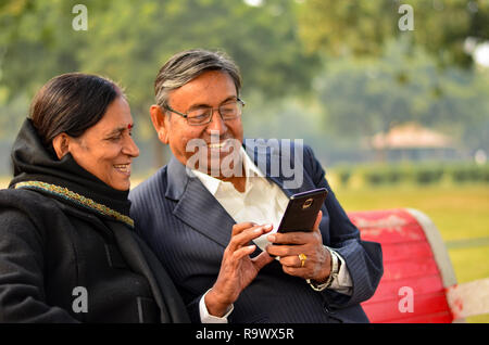 Couple travaillant sur mobile et à parler, sourire, rire dans un parc en hivers à Delhi, Inde Banque D'Images