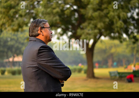 D'un côté indien senior homme portant un costume dans l'extérieur de l'établissement comité permanent et souriant dans un parc à New Delhi, Inde Banque D'Images