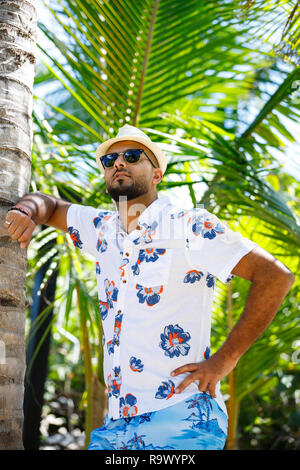 Tourisme à la mode homme en short et chemise à fleurs debout sous les cocotiers Banque D'Images