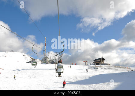 Femme en blanc d'hiver, une veste équitation les pentes au-dessus de la société, les gens skier avec l'ascenseur, une tour de communications sur le sommet de la montagne Banque D'Images