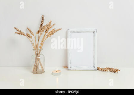 Maquette du châssis vertical avec seigle sauvage bouquet en vase en verre près de mur blanc. Cadre vide maquette pour sa présentation. Pour l'ossature du modèle ar moderne Banque D'Images