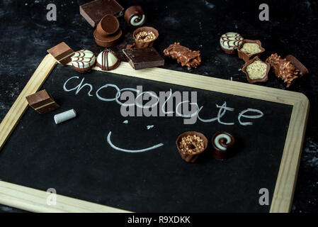 Doux, différent de pralines, sombre et du lait au chocolat blanc sur un fond de bois sombre,, à côté du tableau avec le mot chocolat Banque D'Images