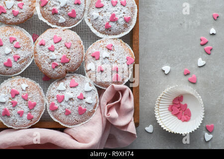 Muffins saupoudrés de sucre à glacer et rose fondant blanc coeurs. Vue de dessus, un anniversaire ou la Saint Valentin concept. Banque D'Images