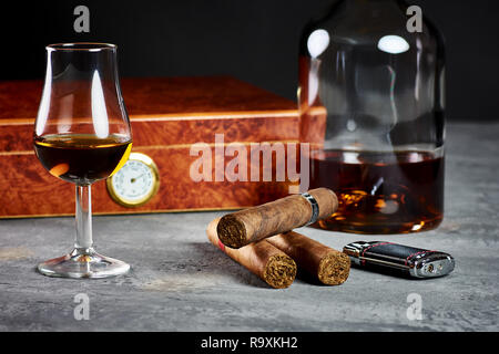 Trois cigares cubains sur une table en pierre avec un briquet et une cave à cigares en bois, un verre et une bouteille de whisky. Banque D'Images