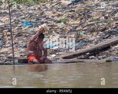 Iquitos, Pérou - Sep 25, 2018 : l'homme est assis sur les rives de la rivière Itaya et refroidit son corps avec de l'eau. Une énorme pollution de l'air peut être vu dans le backgrou Banque D'Images