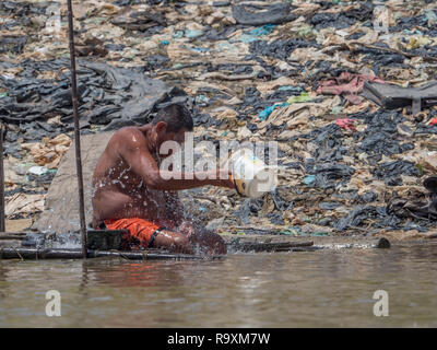 Iquitos, Pérou - Sep 25, 2018 : l'homme est assis sur les rives de la rivière Itaya et refroidit son corps avec de l'eau. Une énorme pollution de l'air peut être vu dans le backgrou Banque D'Images